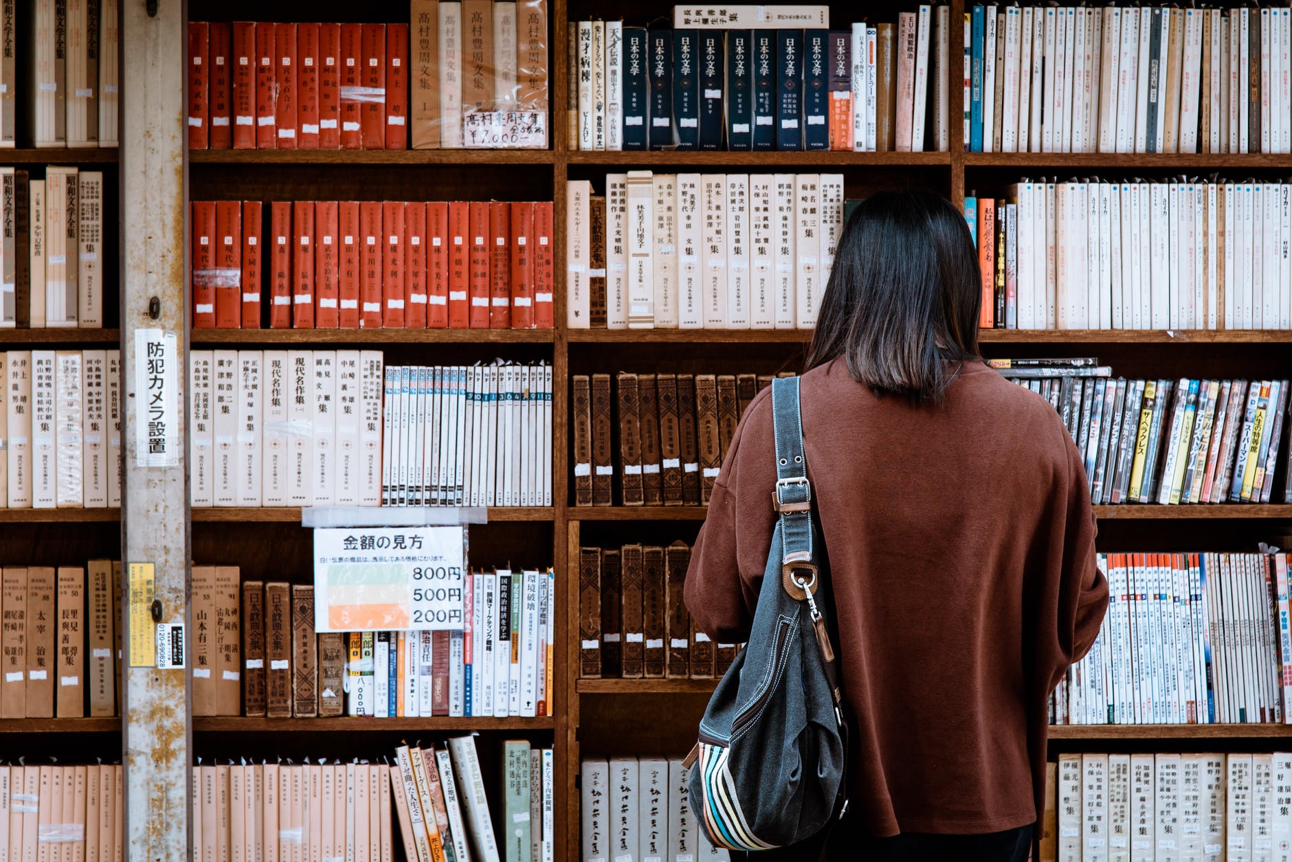 woman wearing brown shirt carrying black leather bag on front of library books