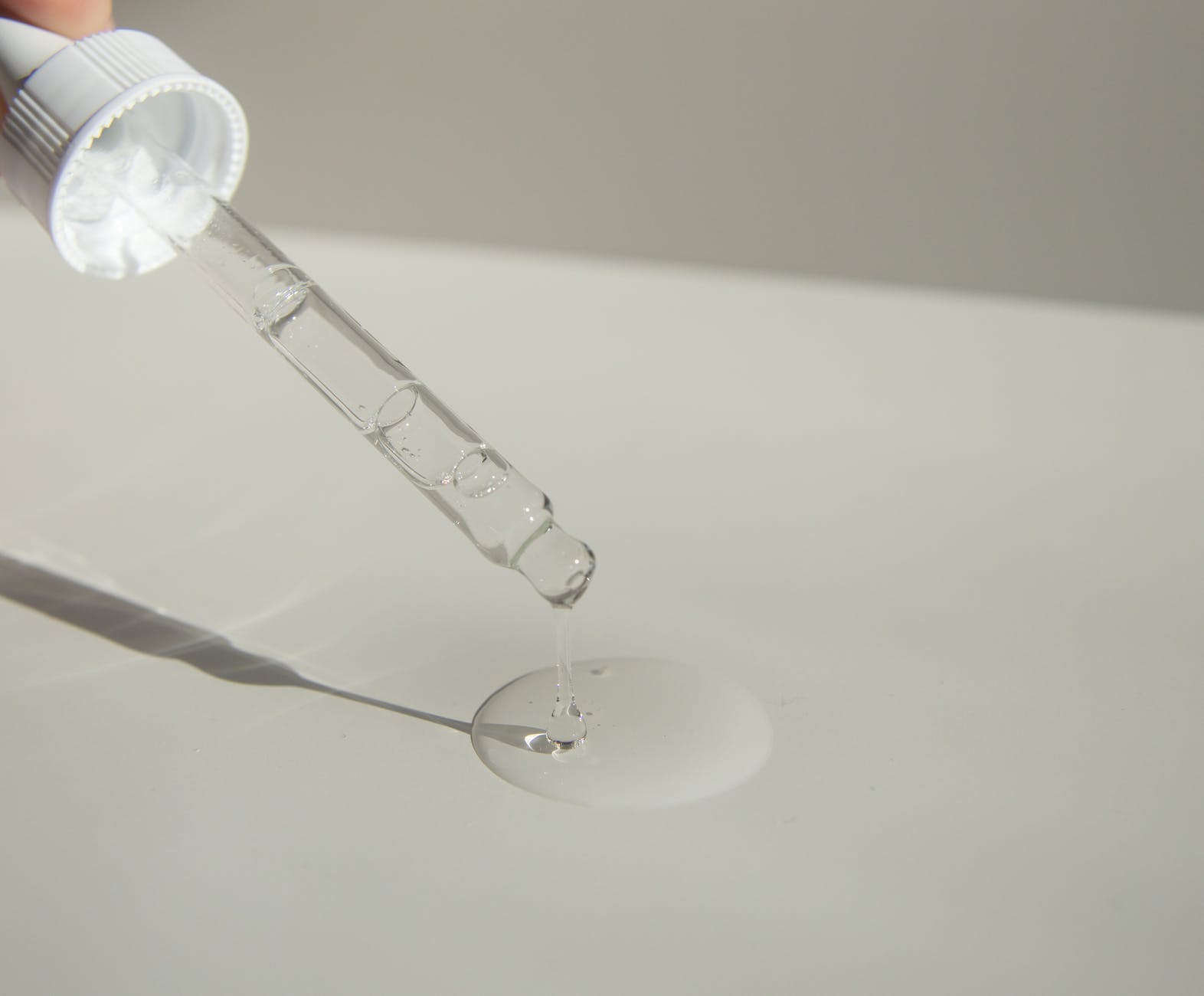 anonymous person pouring liquid product on table with pipette