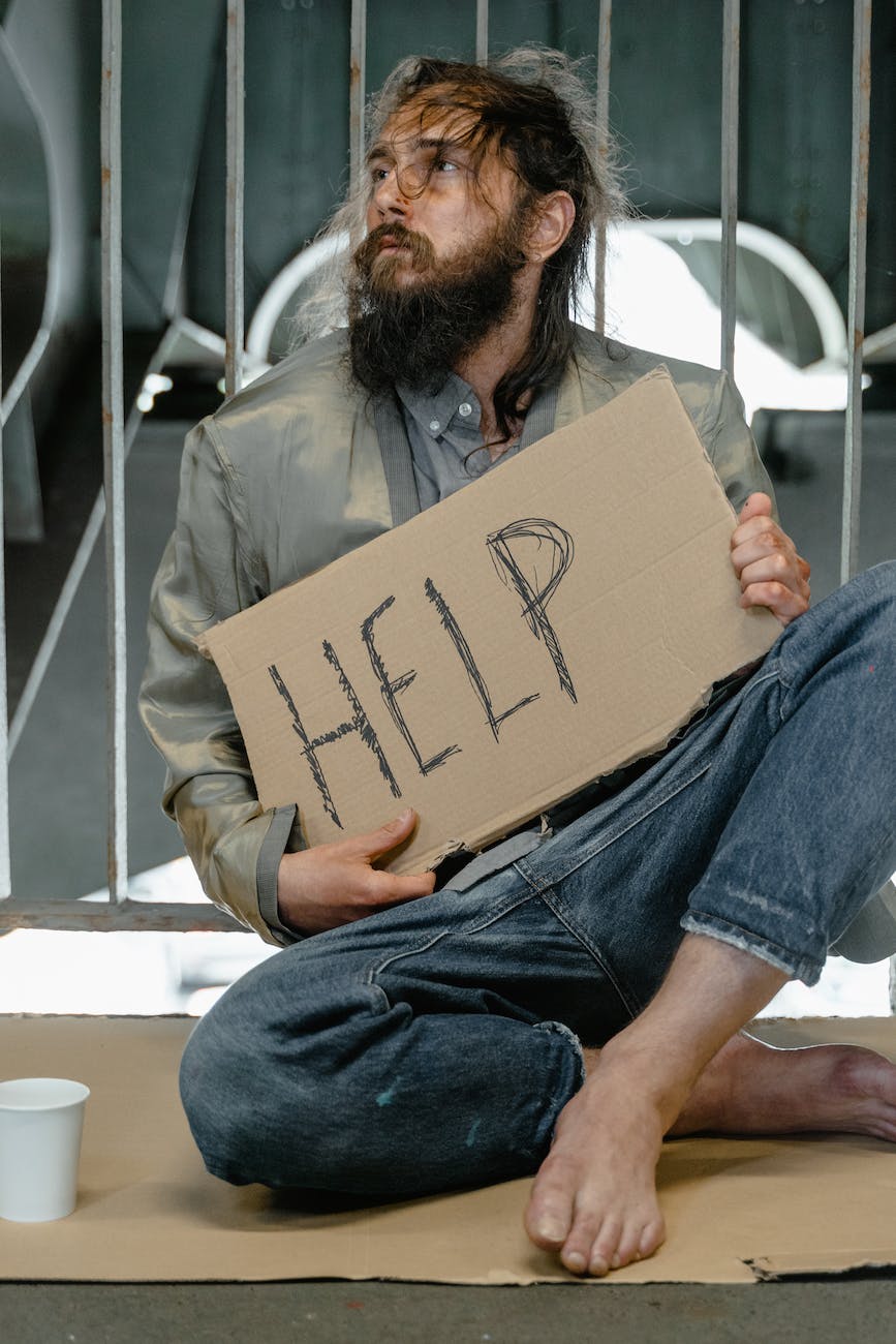 a male beggar sitting on a ground while holding a help banner